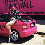 ADELA posing with a pink car in front of a pink wall