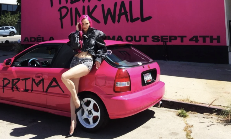 ADELA posing with a pink car in front of a pink wall